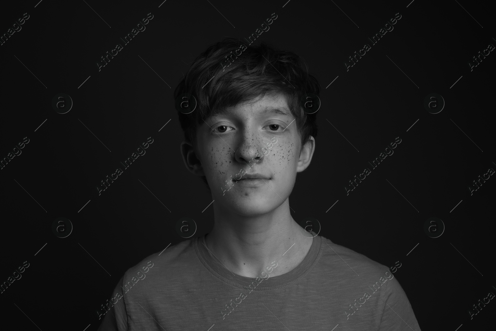 Photo of Teenage boy with freckles on dark background, black and white effect