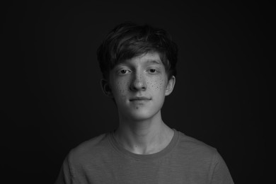 Photo of Teenage boy with freckles on dark background, black and white effect