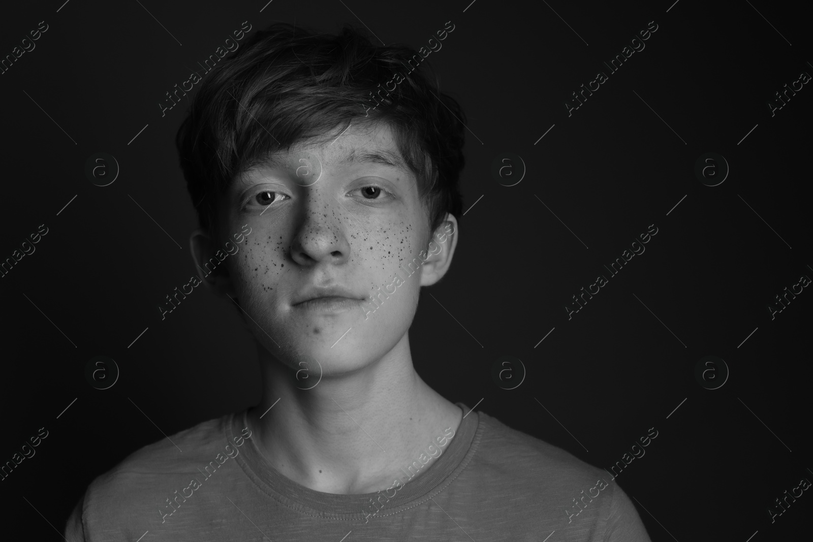 Photo of Teenage boy with freckles on dark background, black and white effect