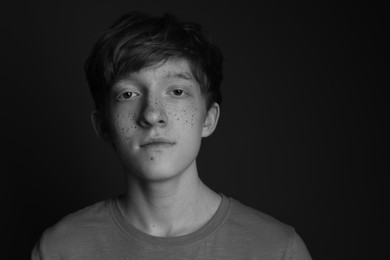 Photo of Teenage boy with freckles on dark background, black and white effect