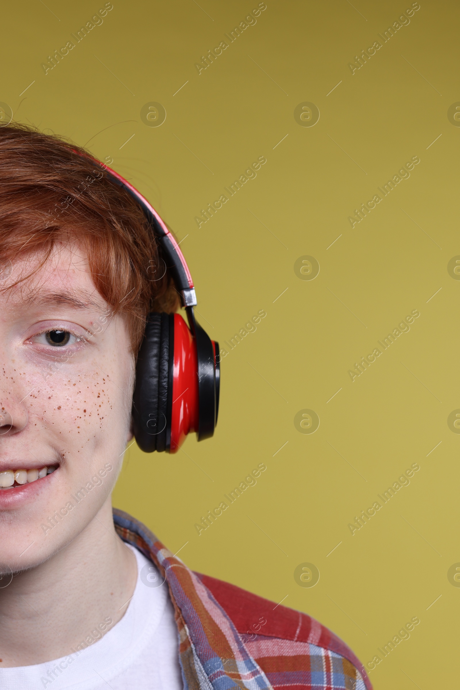 Photo of Smiling teenage boy with freckles listening to music by headphones on yellow background, closeup. Space for text