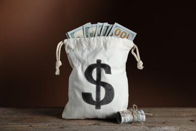 Photo of Burlap sack with dollar banknotes on wooden table against brown background