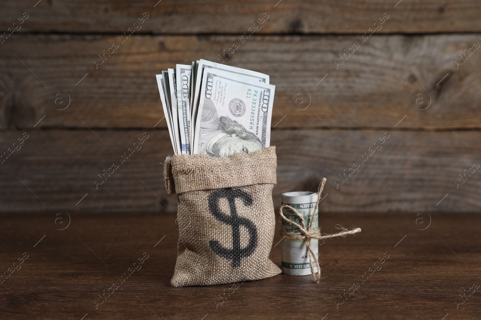 Photo of Burlap sack with dollar banknotes on wooden table