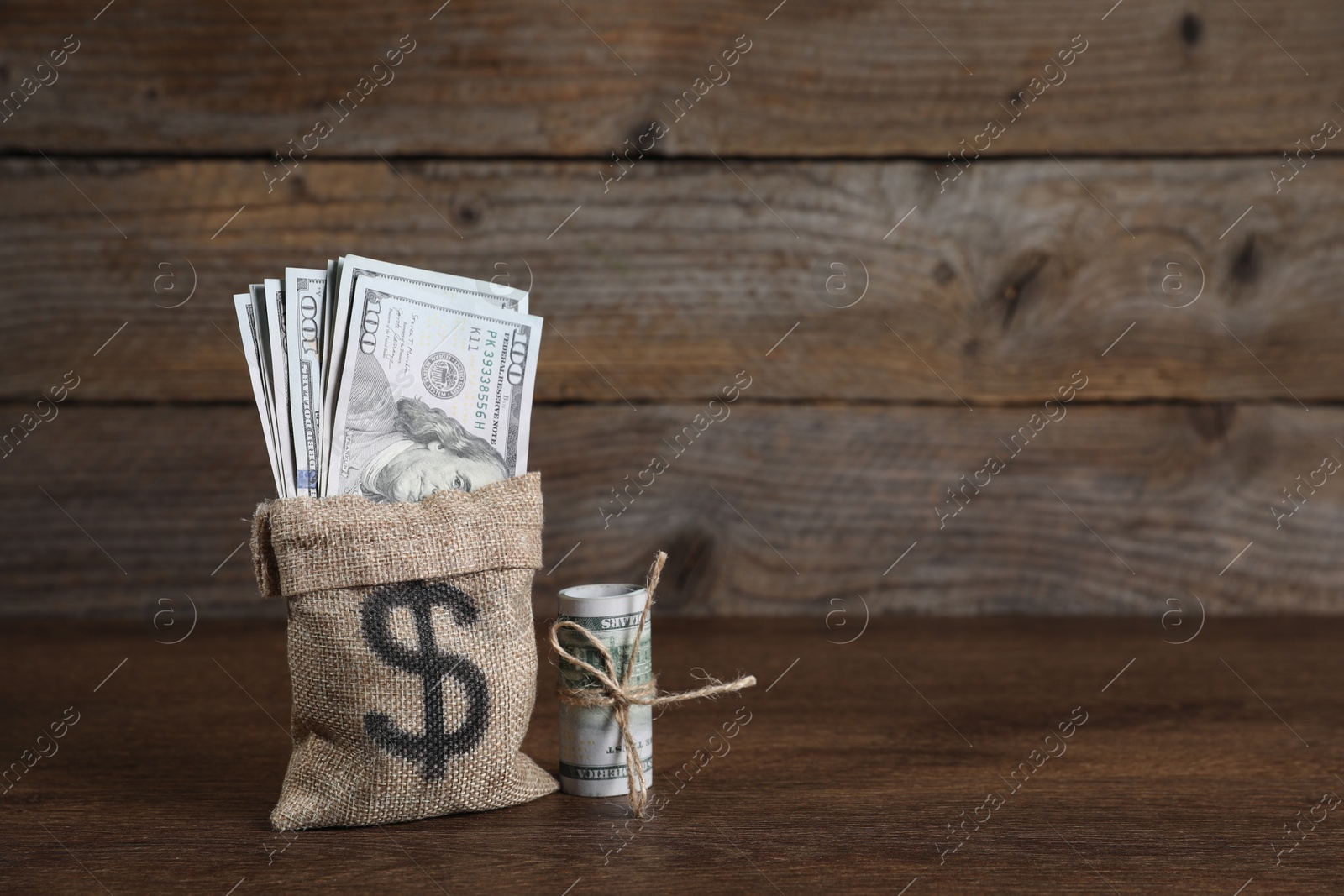 Photo of Burlap sack with dollar banknotes on wooden table, space for text