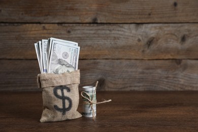 Photo of Burlap sack with dollar banknotes on wooden table, space for text