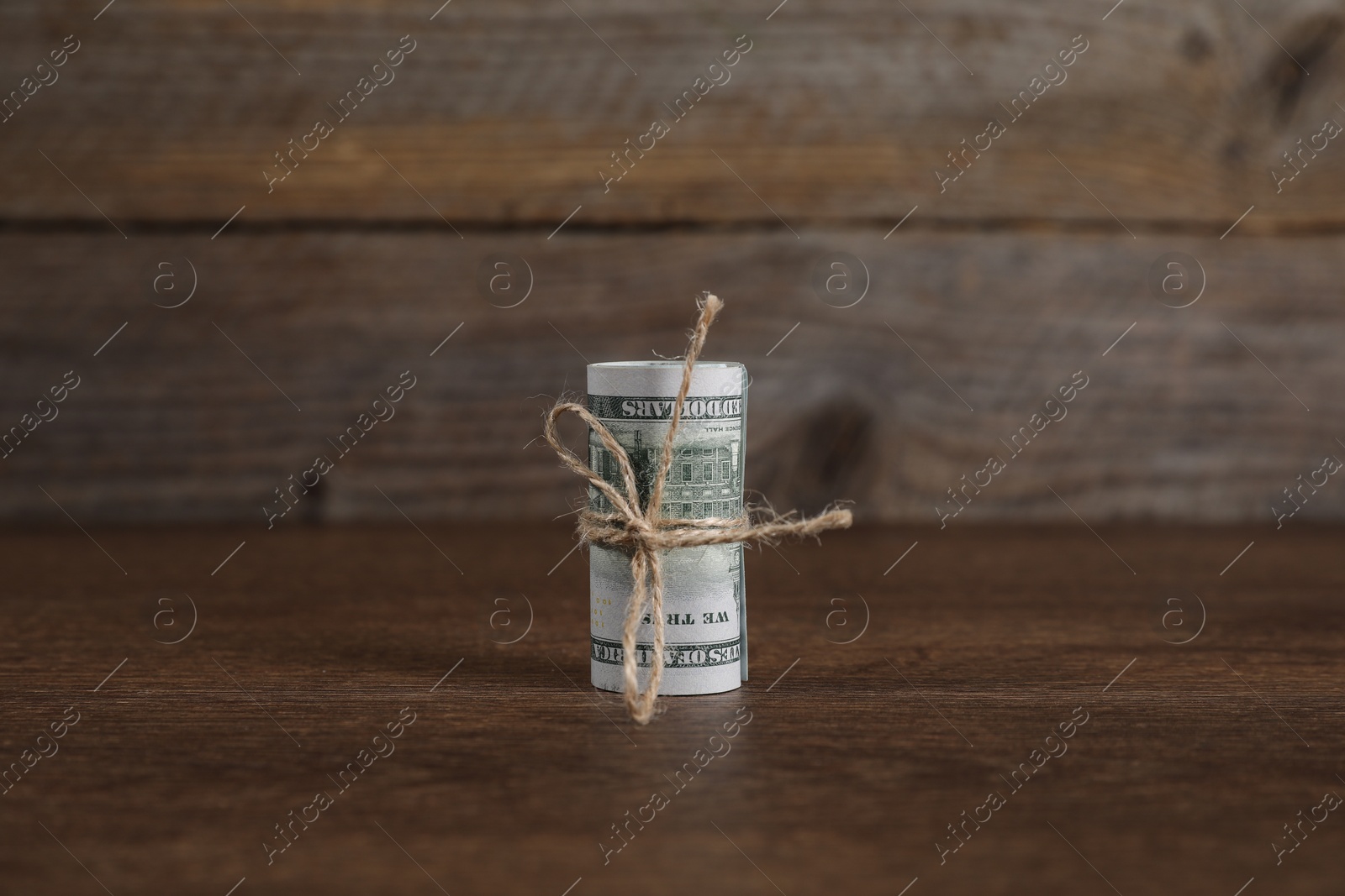 Photo of Rolled dollar banknotes with rope on wooden table