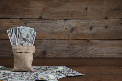 Photo of Burlap sack with dollar banknotes on wooden table, space for text