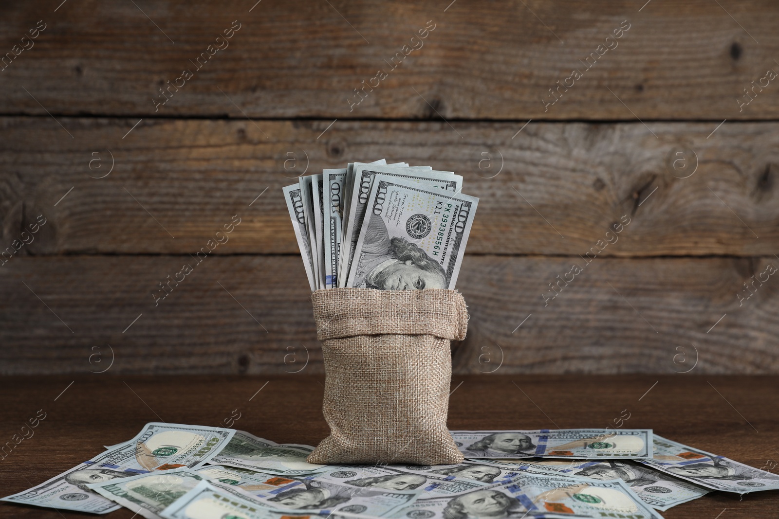 Photo of Burlap sack with dollar banknotes on wooden table