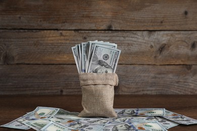 Photo of Burlap sack with dollar banknotes on wooden table