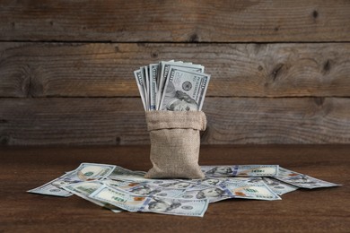 Photo of Burlap sack with dollar banknotes on wooden table