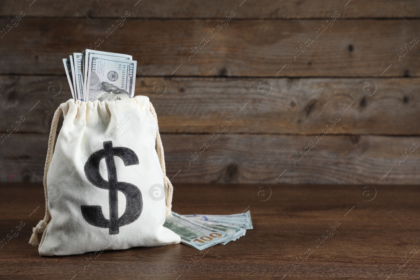 Photo of Dollar banknotes in burlap sack on wooden table, space for text