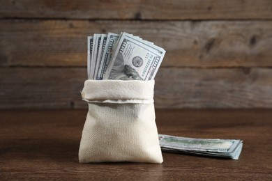 Photo of Burlap sack with dollar banknotes on wooden table