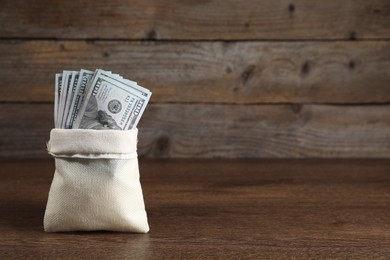 Photo of Dollar banknotes in burlap sack on wooden table, space for text