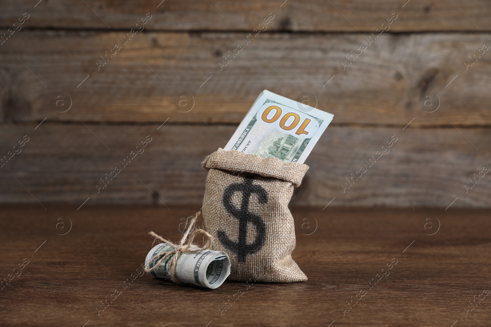 Photo of Burlap sack with dollar banknotes on wooden table