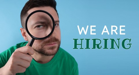 Image of We are hiring. Man looking through magnifying glass on light blue background, banner design. Human resource, recruitment concept