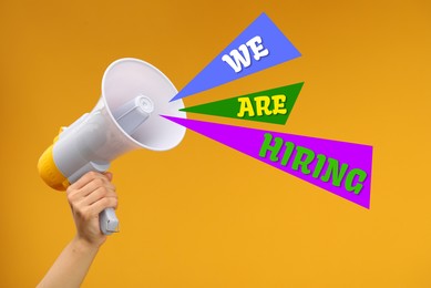 Image of We Are Hiring words coming out of megaphone in woman's hand on orange background, closeup. Human resource, recruitment concept