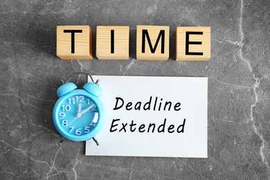 Image of Paper with text Deadline Extended, alarm clock and word Time made on wooden cubes on grey marble table, flat lay