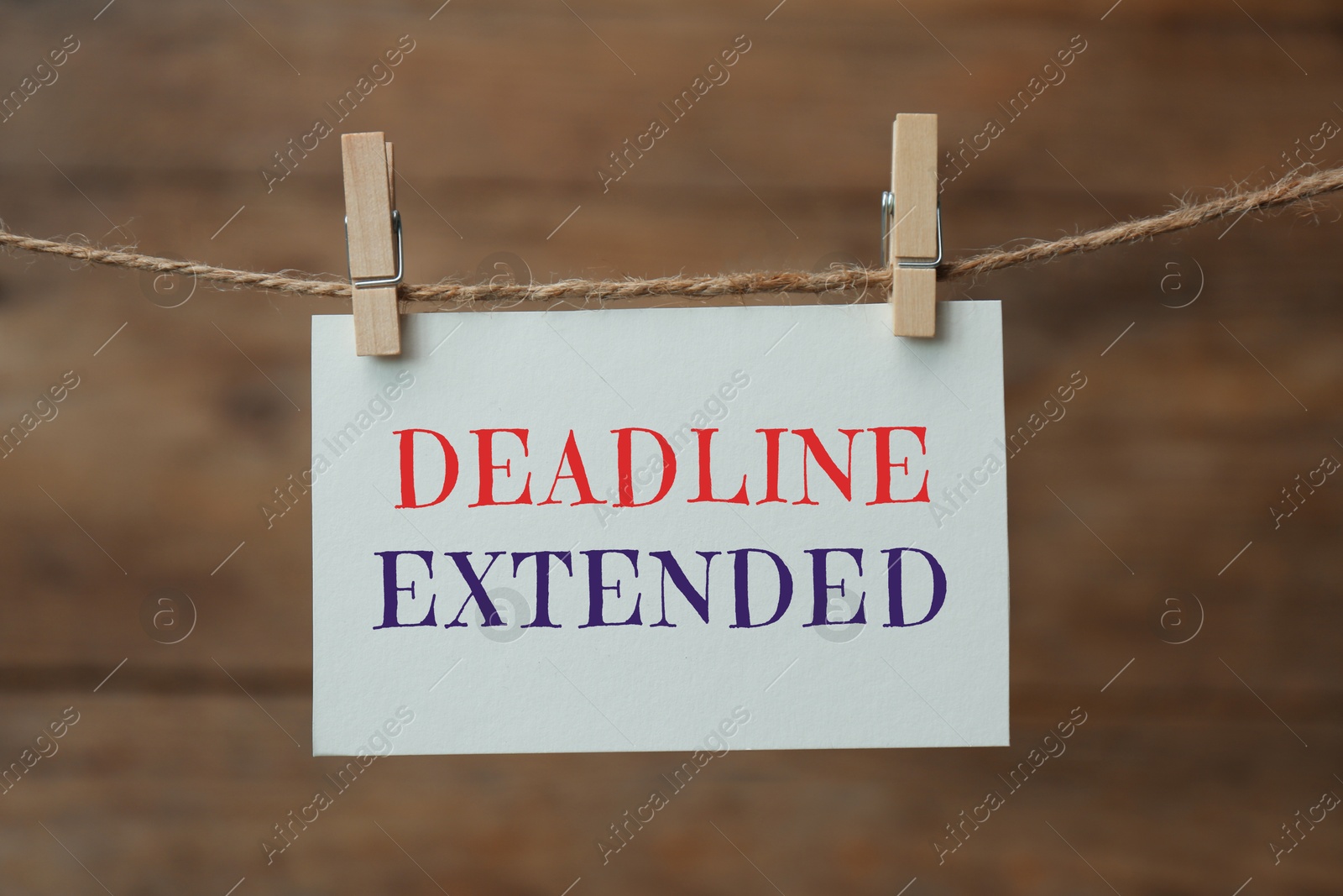 Image of Paper note with text Deadline Extended hanging on rope against wooden wall