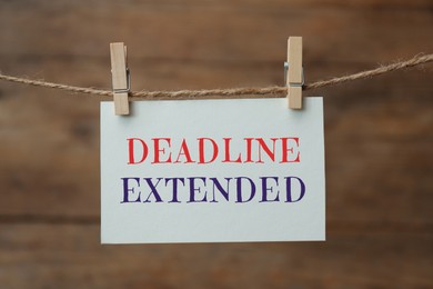 Image of Paper note with text Deadline Extended hanging on rope against wooden wall