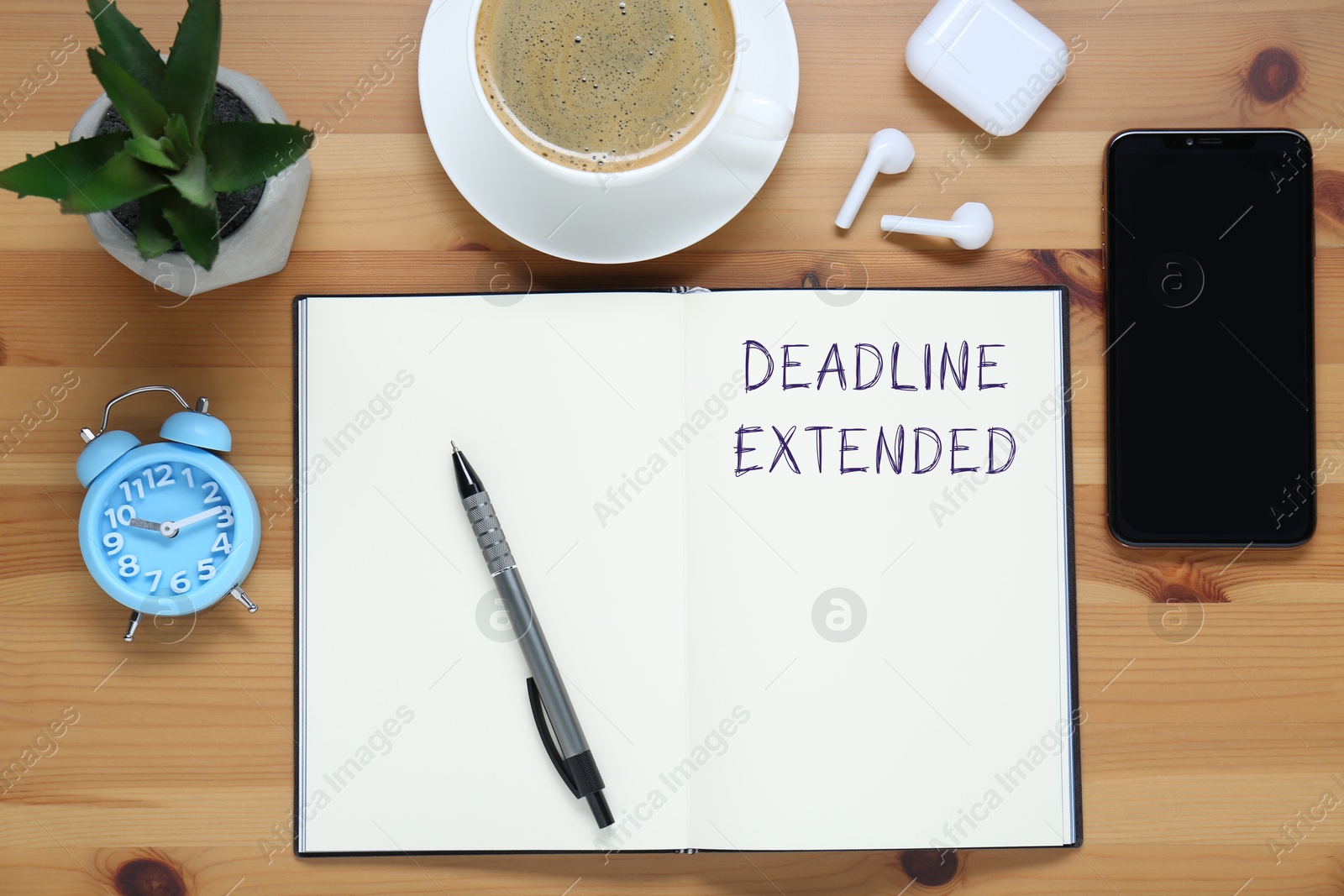 Image of Text Deadline Extended in notebook, pen, alarm clock, mobile phone, earphones and coffee on wooden table, flat lay