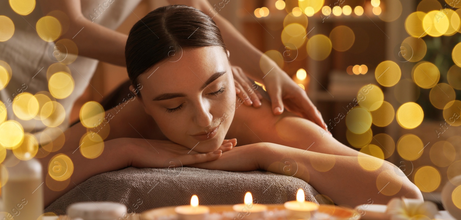 Image of Beautiful young woman lying on table during massage in salon, bokeh effect. Banner design