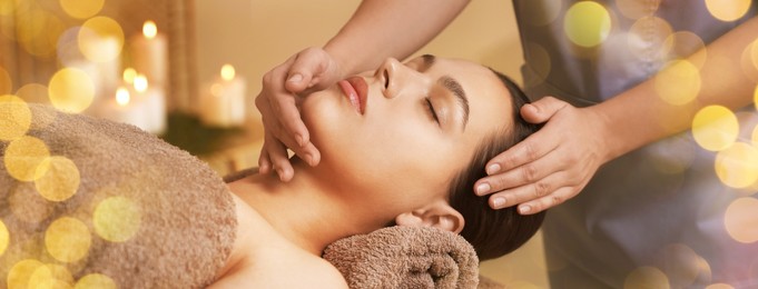 Image of Beautiful young woman receiving face massage in spa salon, bokeh effect. Banner design