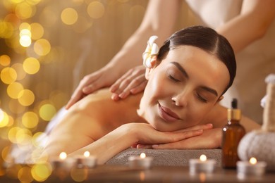 Image of Beautiful young woman lying on table during massage in salon, bokeh effect