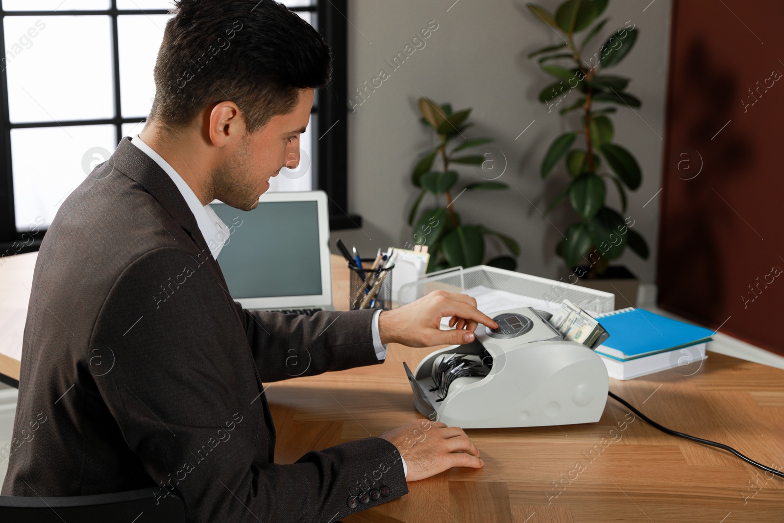 Photo of Man using banknote counter at wooden table indoors