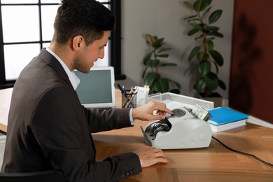 Photo of Man using banknote counter at wooden table indoors