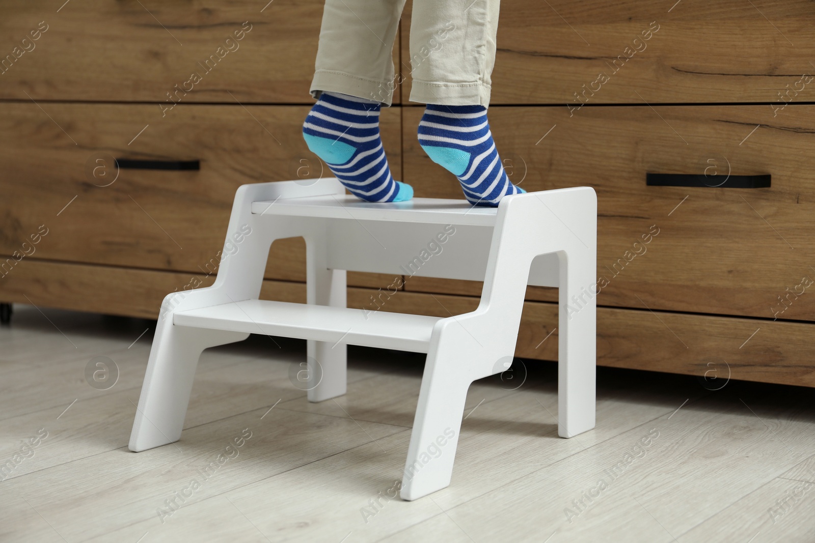 Photo of Little boy standing on step stool near chest of drawers at home, closeup