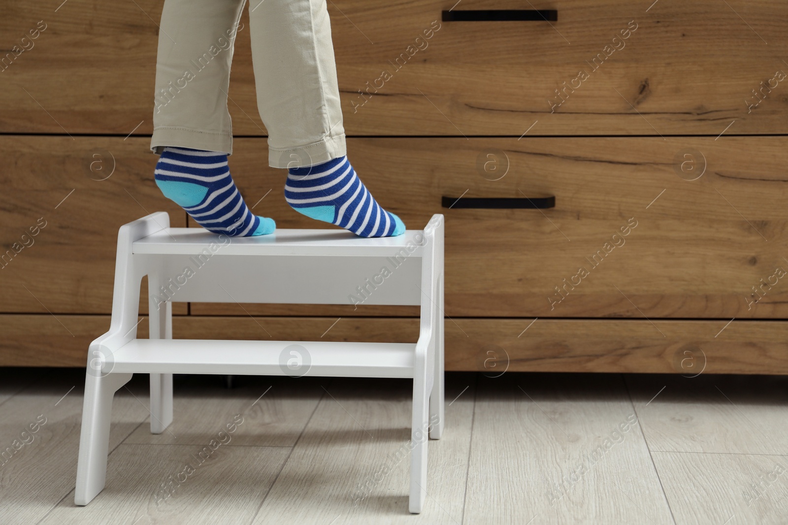 Photo of Little boy standing on step stool near chest of drawers at home, closeup. Space for text