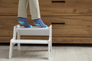 Photo of Little boy standing on step stool near chest of drawers at home, closeup. Space for text