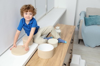 Photo of Little boy with boxes on window sill at home