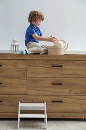 Photo of Little boy with boxes on window sill and step stool at home