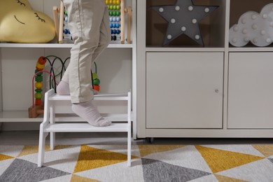 Photo of Little boy standing on step stool at home, closeup