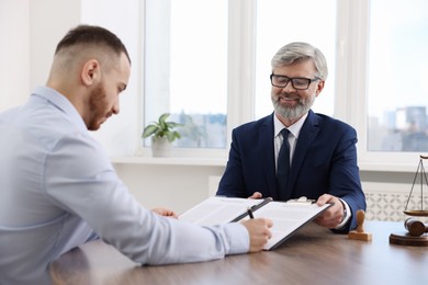 Client signing notarial paperwork during meeting with lawyer at wooden desk indoors