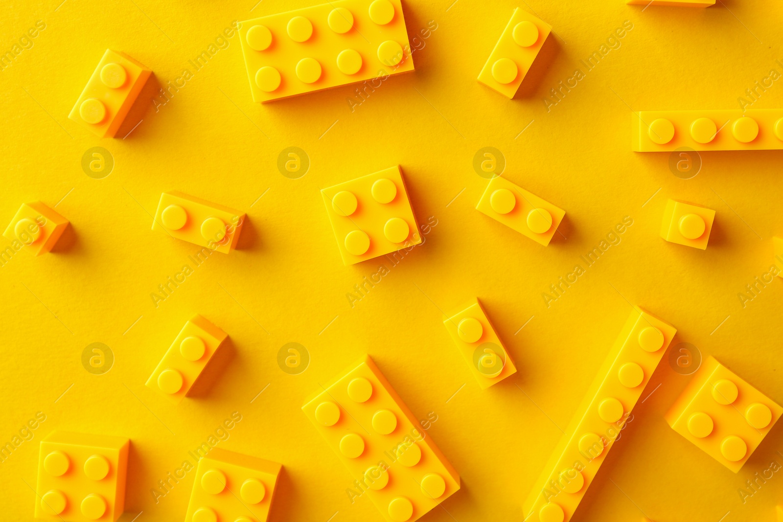 Photo of Constructor toy. Many building blocks on yellow background, flat lay