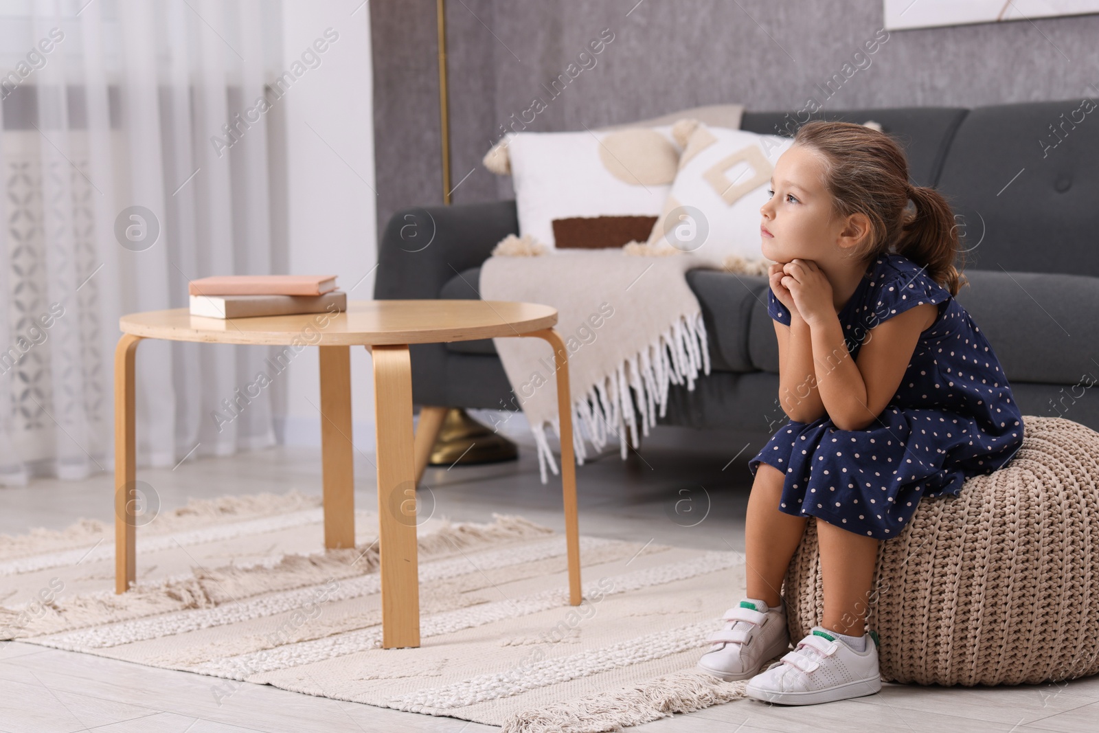 Photo of Resentful little girl sitting on pouf at home, space for text