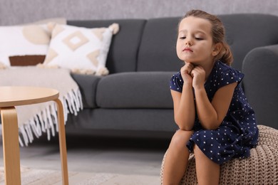 Photo of Resentful little girl sitting on pouf at home, space for text