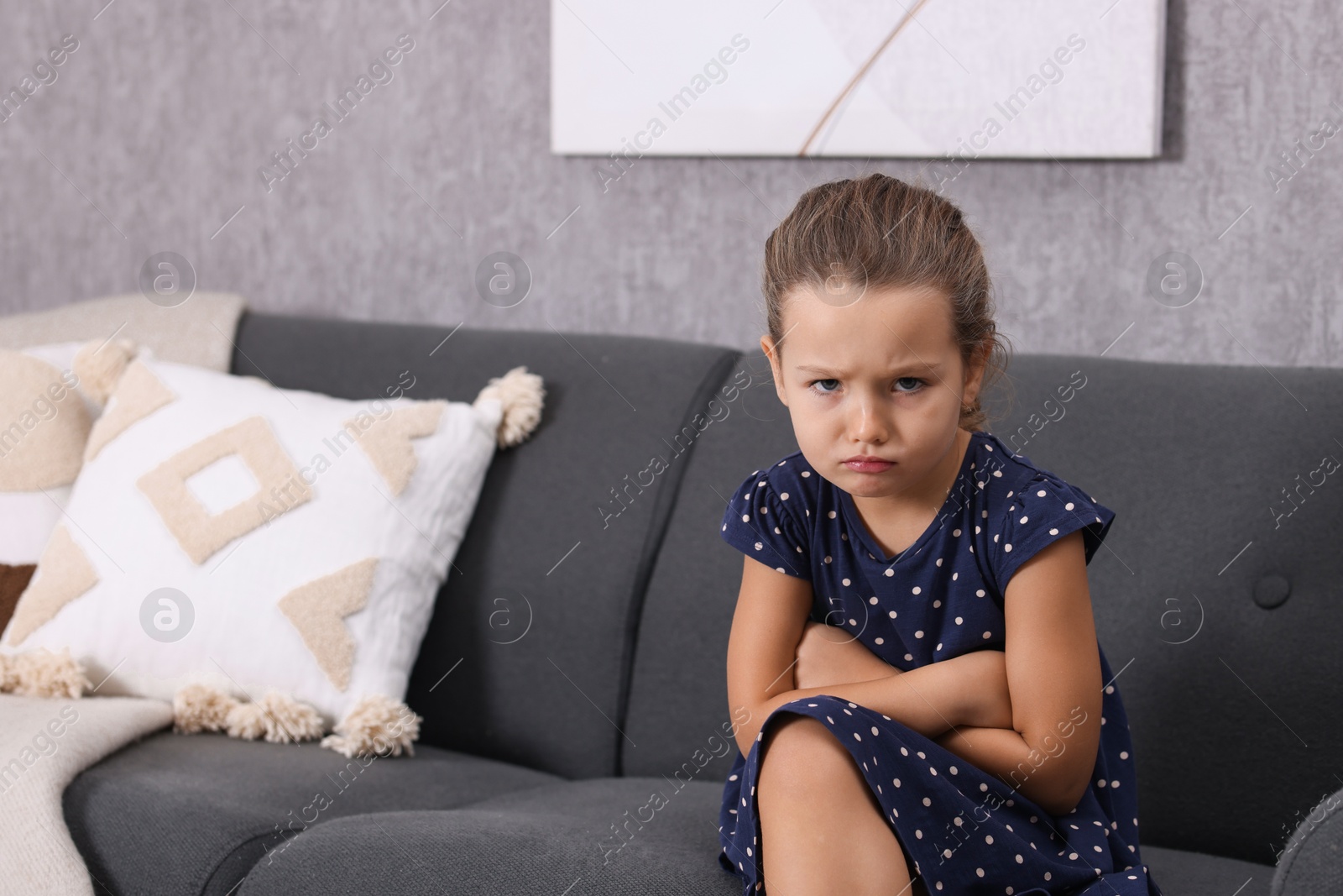 Photo of Resentful little girl sitting on couch at home, space for text