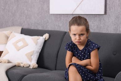 Photo of Resentful little girl sitting on couch at home, space for text