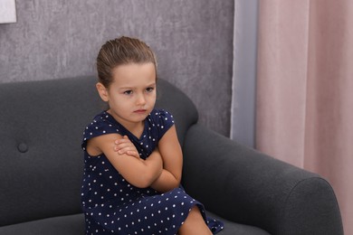 Photo of Resentful little girl sitting on couch at home, space for text