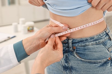 Photo of Weight loss. Nutritionist measuring patient's waist with tape in clinic, closeup