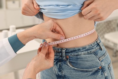 Photo of Weight loss. Nutritionist measuring patient's waist with tape in clinic, closeup