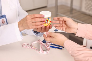 Photo of Weight loss. Nutritionist giving medical bottle with pills to patient at table in clinic, closeup