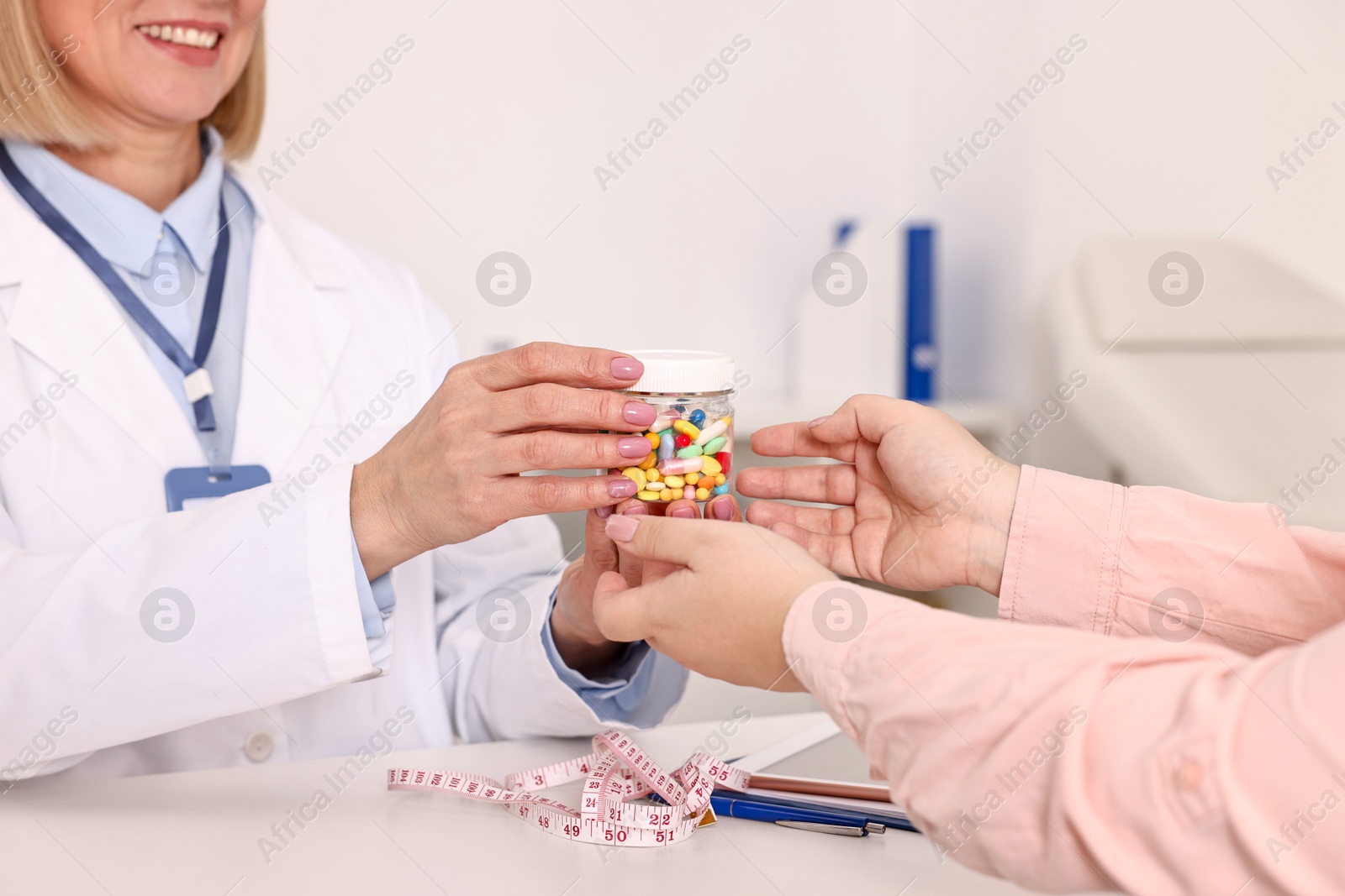 Photo of Weight loss. Smiling nutritionist giving medical bottle with pills to patient at table in clinic, closeup