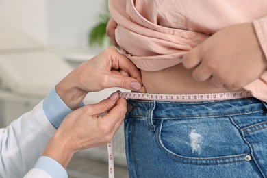 Photo of Weight loss. Nutritionist measuring patient's waist with tape in clinic, closeup