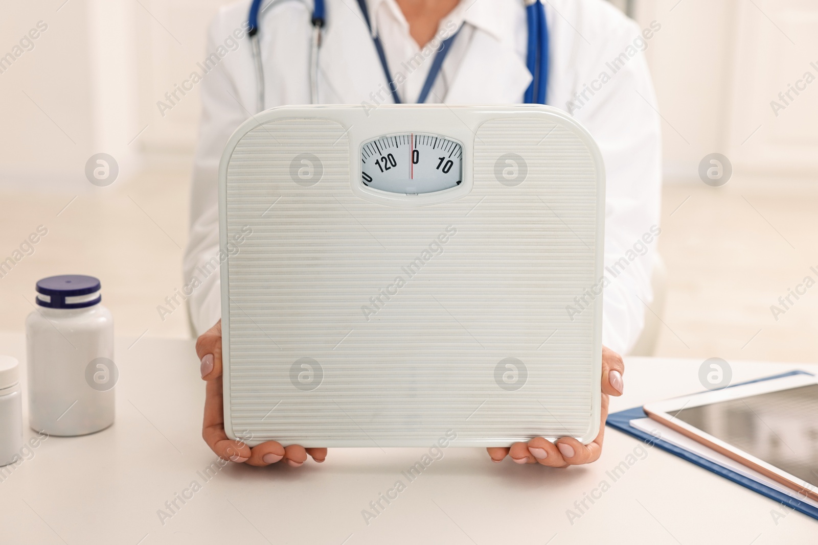 Photo of Weight loss. Nutritionist with scales at table in clinic, closeup