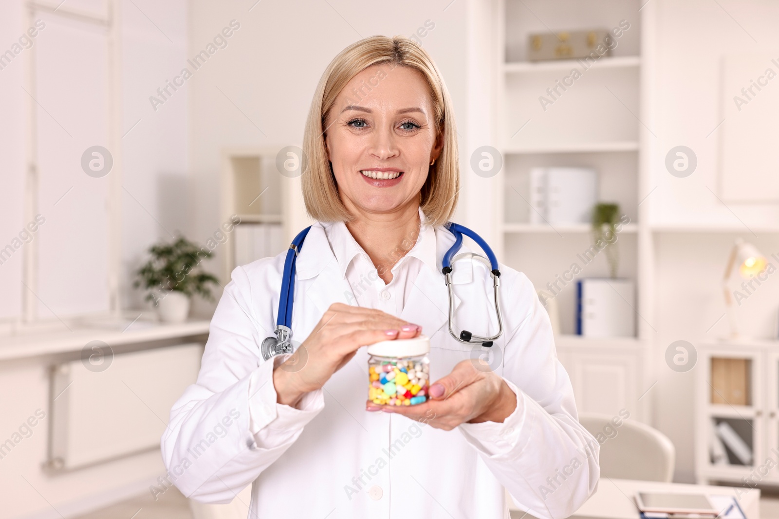 Photo of Happy nutritionist with container of weight loss pills in clinic