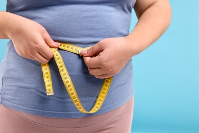 Photo of Weight loss. Plus size woman measuring waist with tape on light blue background, closeup